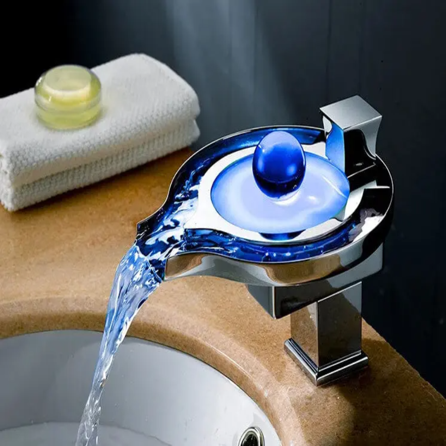 Chrome faucet with blue light pouring water into a sink, with a towel and soap in the background.